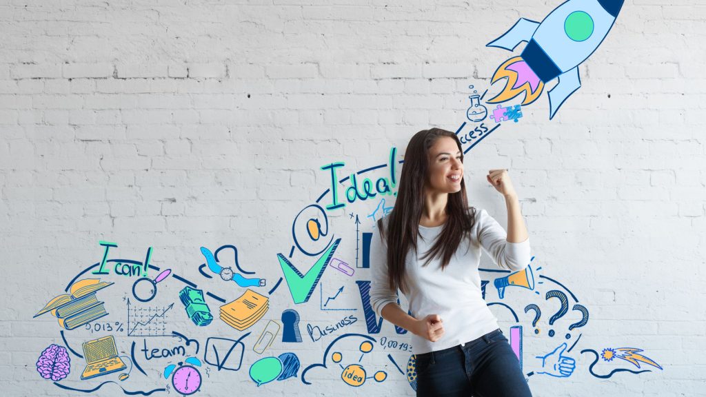 A photo of a person standing in front of wall with script indicating success and entrepreneurship. The person looks determined and confident, holding their fist to the sky and a big smile on their face.