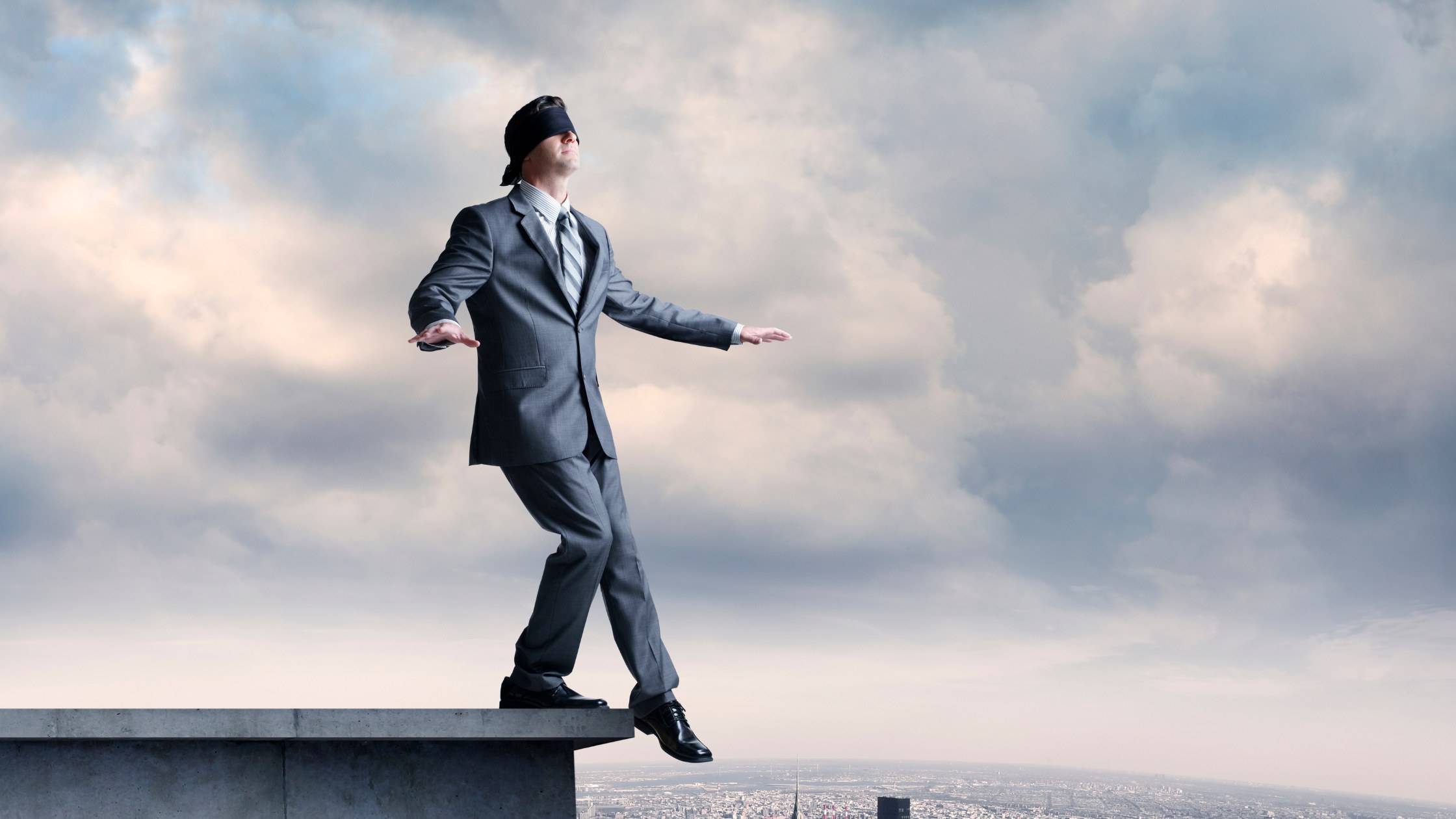 Blindfolded man walking toward the edge of a building, symbolising risk of driving a business without systems and direction